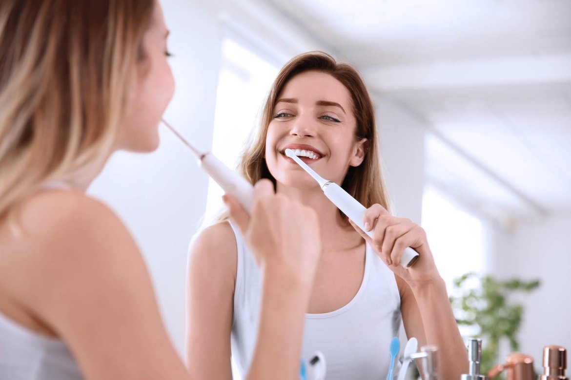 zu sehen ist eine Frau mit einer elektischen Zahnbürste